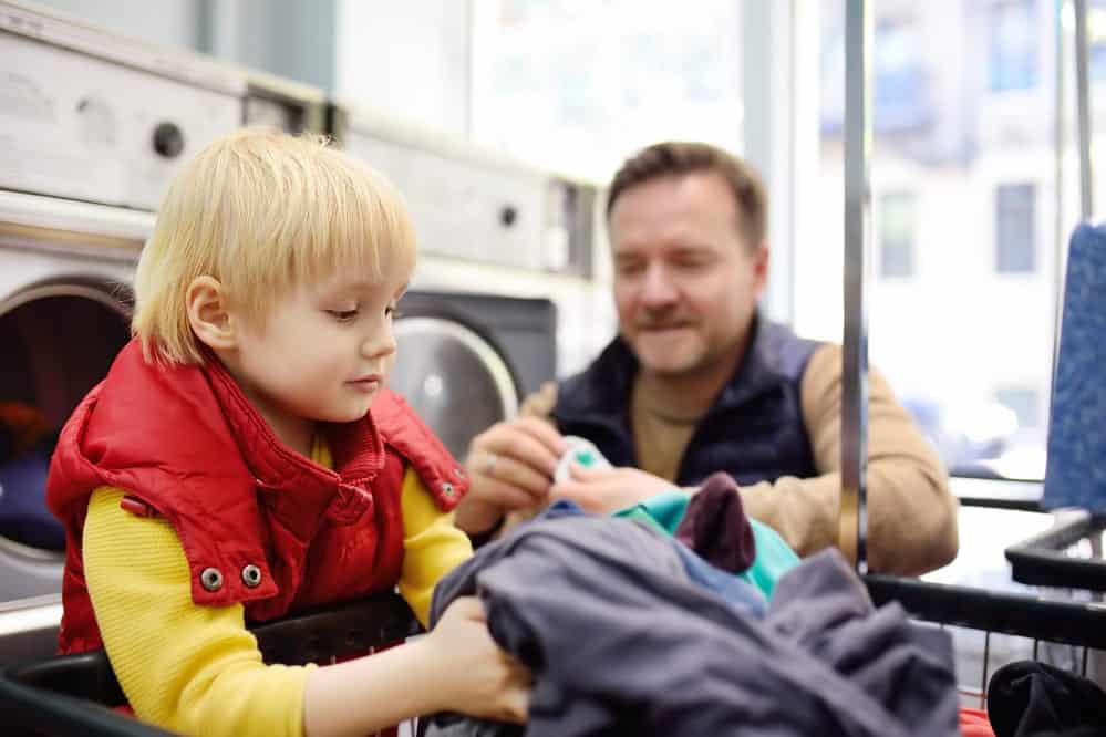 A little boy loads clothes into the washing machine in public laundromat