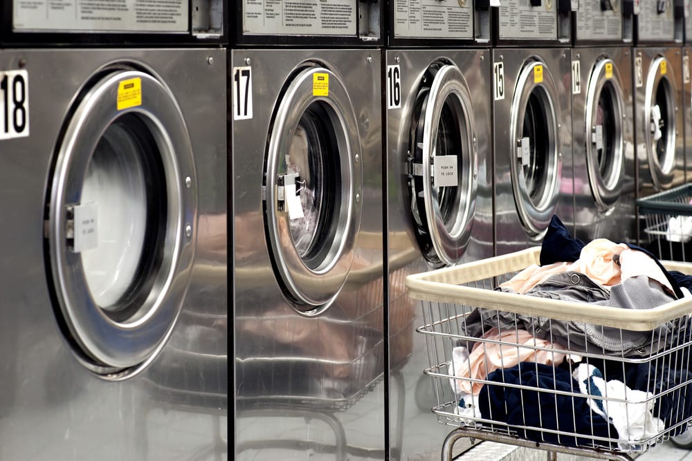 A row of industrial washing machines in a public laundromat, with laundry in a basket