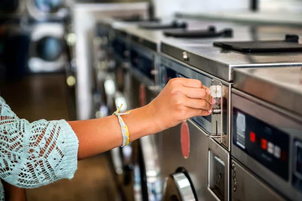 Close-up of hand inserting coin into laundry machine at laundromat