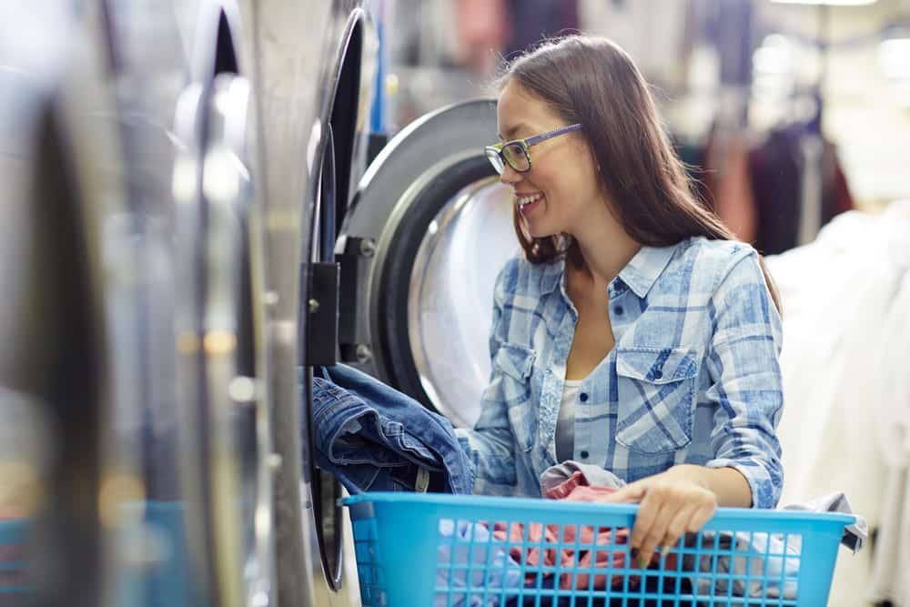 Young woman putting clothes into washing machine at laundromat