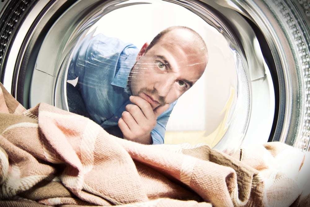 Shot from inside the dryer, man looking inside at dry towels with uncertain expression
