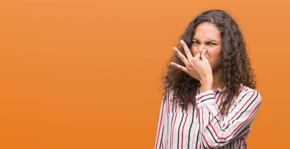 Woman holding nose at stinky odor, orange background
