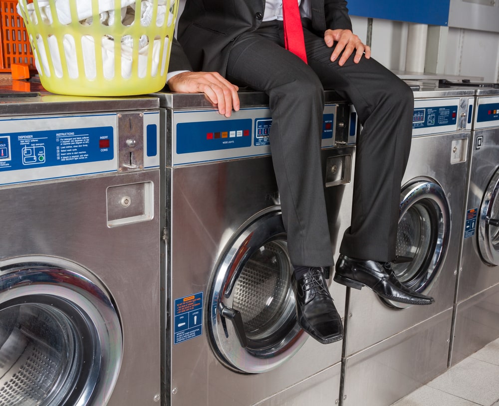 Man in business suit sitting on washing machine in laundromat