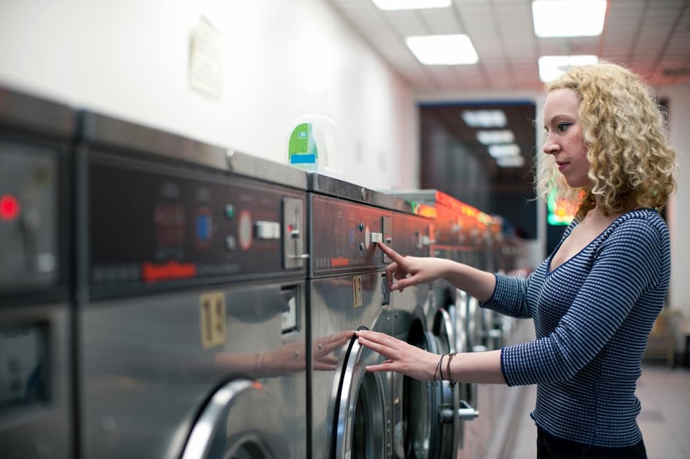 Woman pressing button on washing machine in laundromat